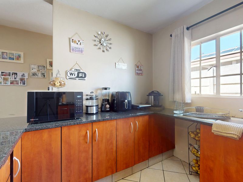 A functional kitchen featuring wooden cabinetry, granite countertops, and a stainless steel sink, with natural light provided by a window.