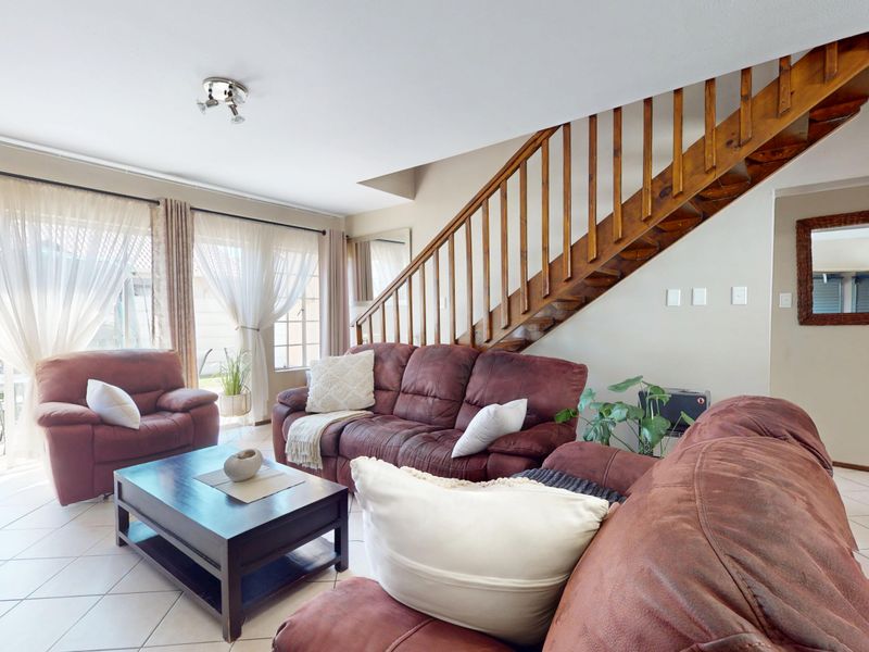 Spacious living room featuring tiled flooring, a wooden staircase, and large sliding glass doors providing natural light and access to the exterior.