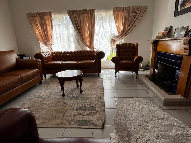 A comfortable living room featuring tiled flooring, a traditional fireplace with a wooden mantel, and a ceiling fan.