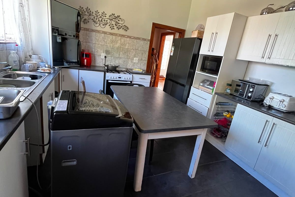 A functional kitchen featuring white cabinetry, tiled backsplash, built-in oven and hob, and dark tiled flooring, offering a practical layout for daily meal preparation.