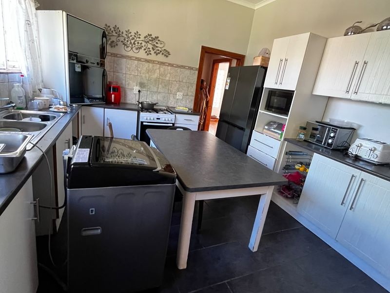 A functional kitchen featuring white cabinetry, tiled backsplash, built-in oven and hob, and dark tiled flooring, offering a practical layout for daily meal preparation.