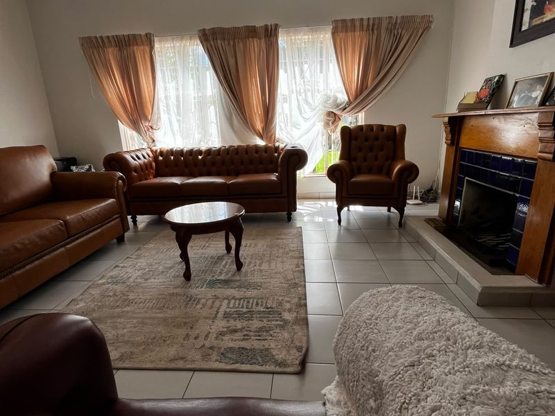 A spacious living room featuring tiled flooring, a traditional fireplace with a wooden mantel, and a ceiling fan.