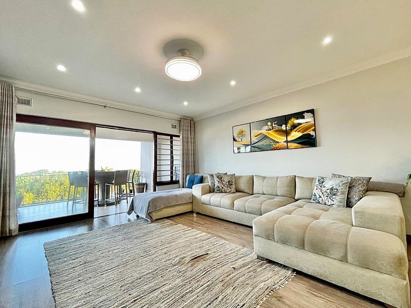 A bright and spacious living room featuring laminate flooring, recessed lighting, and large sliding glass doors that open onto a private balcony.