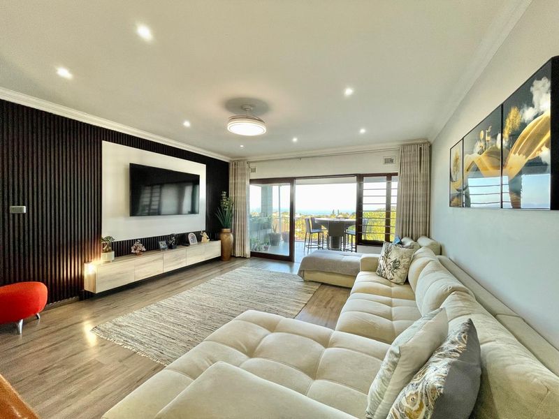 Modern living room featuring a stylish slatted feature wall, floating media console, recessed lighting, and large sliding doors opening to a balcony with views.