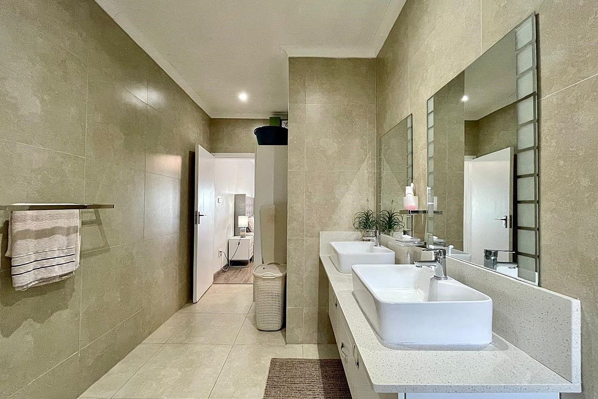 Modern bathroom featuring a double vanity with vessel sinks, stone countertops, large wall-mounted mirrors, and neutral floor-to-ceiling tiling.