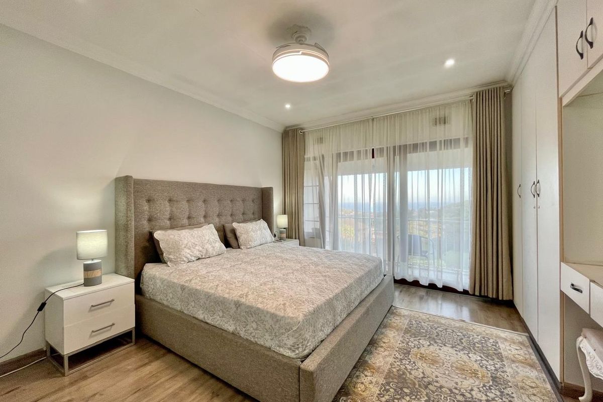 A well-maintained bedroom featuring laminate flooring, built-in cupboards, and a sliding glass door that provides natural light and access to the balcony.