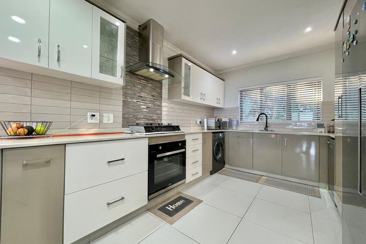 Modern kitchen featuring sleek cabinetry, stone countertops, gas hob, built-in oven, stainless steel extractor, and tiled splashback with integrated sink and downlighting.