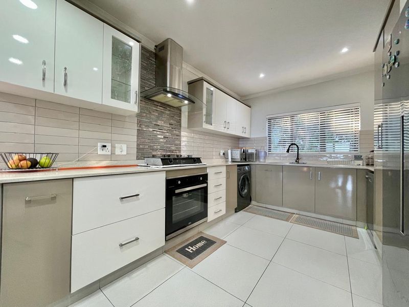 Modern kitchen featuring sleek cabinetry, stone countertops, gas hob, built-in oven, stainless steel extractor, and tiled splashback with integrated sink and downlighting.