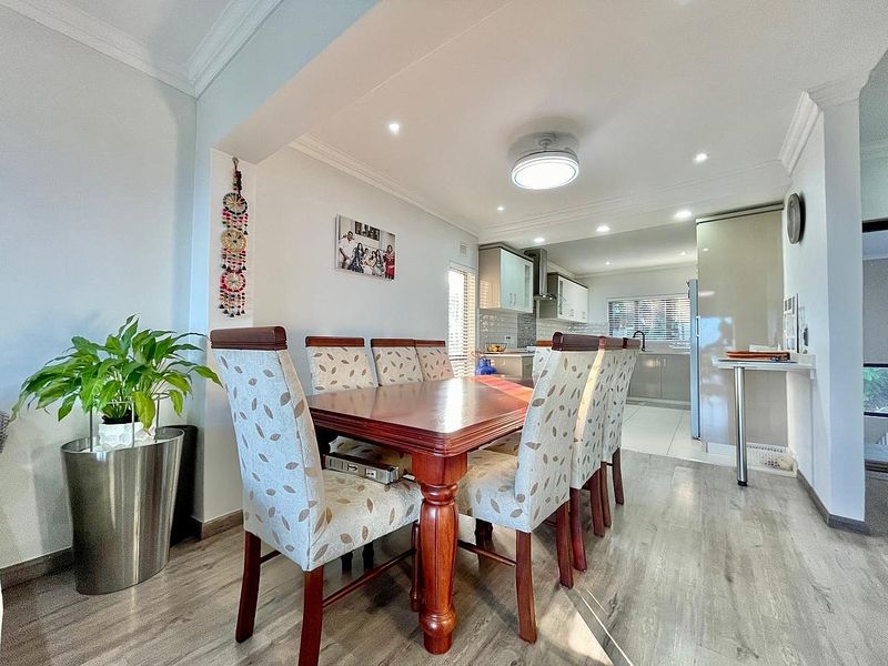 An open-plan dining and kitchen area featuring modern laminate flooring, recessed lighting, and contemporary kitchen cabinetry with a functional breakfast bar.