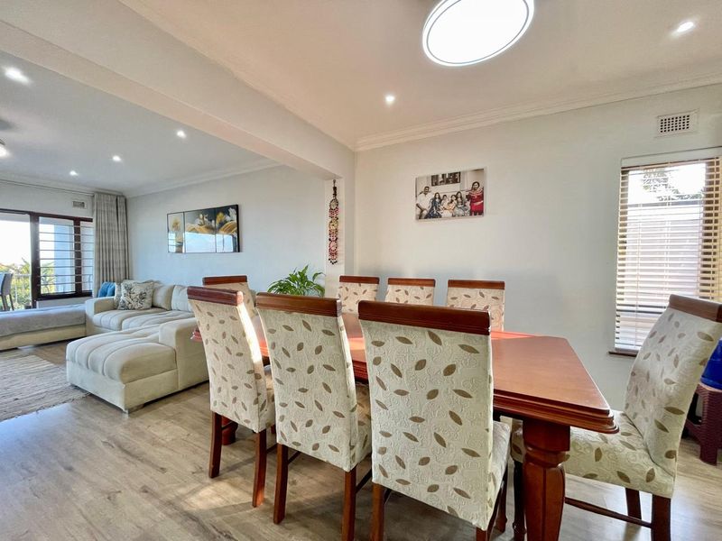Spacious open-plan living and dining area featuring laminate flooring, recessed lighting, and large windows with venetian blinds, creating a bright and inviting atmosphere.