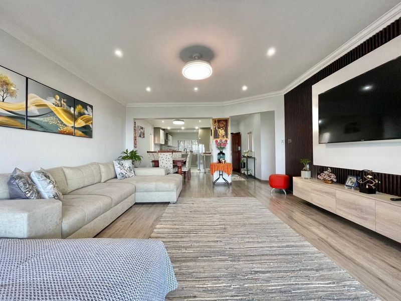 Spacious open-plan living area featuring modern laminate flooring, recessed lighting, and a stylish slatted wood feature wall with an integrated media console.