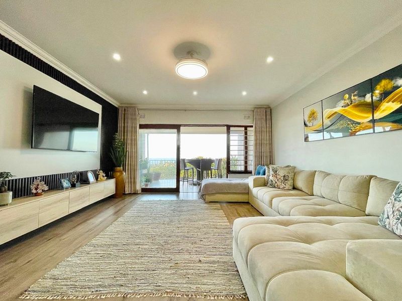 Spacious living room featuring laminate flooring, recessed lighting, and large sliding glass doors that open onto a balcony with scenic views.