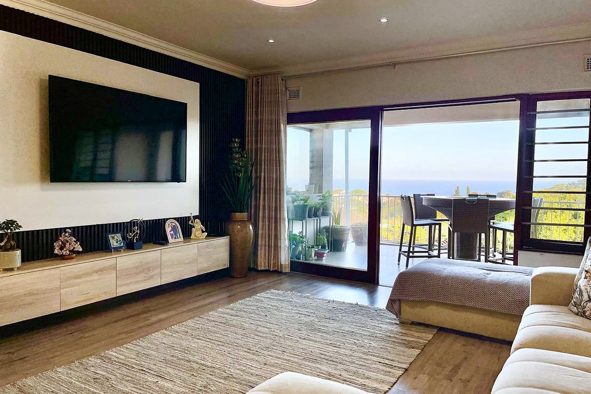 Spacious living room featuring modern slatted wall paneling, built-in media cabinetry, recessed lighting, and large sliding glass doors opening to a scenic balcony.