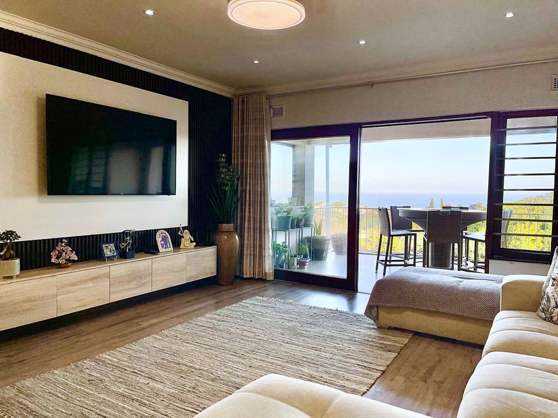 Spacious living room featuring modern slatted wall paneling, built-in media cabinetry, recessed lighting, and large sliding glass doors opening to a scenic balcony.