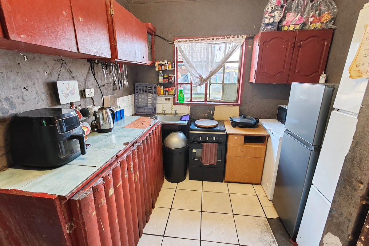 A dated kitchen featuring red cabinetry, tiled countertops, and a freestanding stove, requiring significant cosmetic updates and wall repairs.