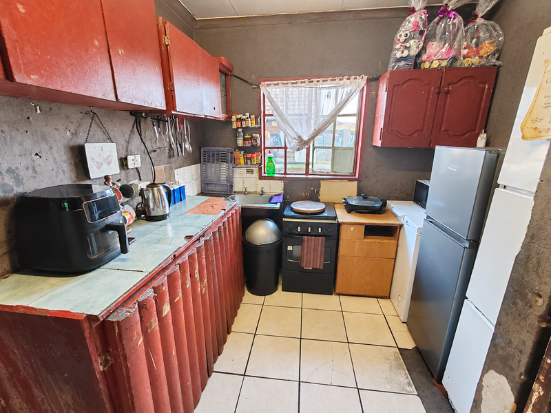 A dated kitchen featuring red cabinetry, tiled countertops, and a freestanding stove, requiring significant cosmetic updates and wall repairs.