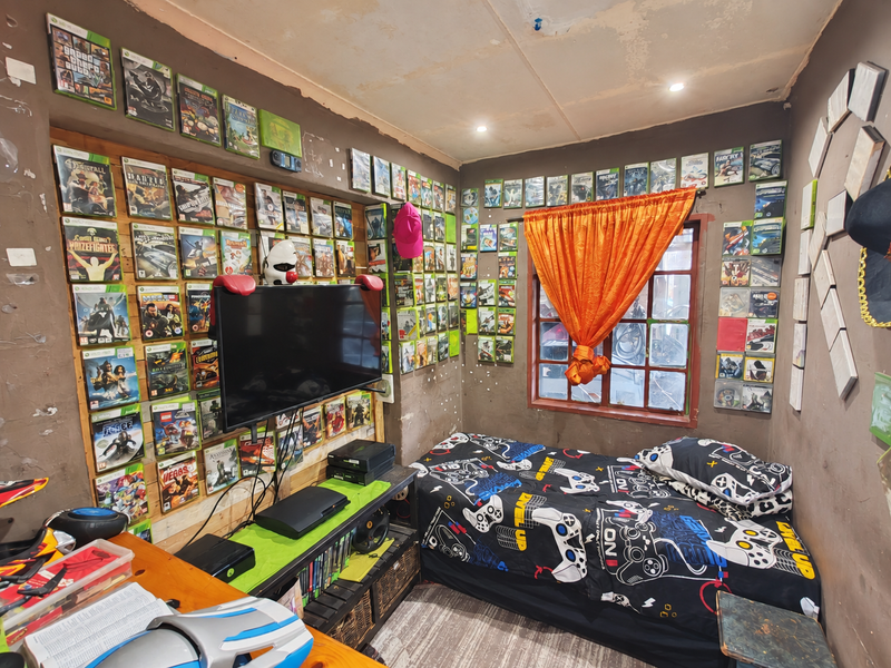 A bedroom featuring a timber-framed window and recessed lighting, currently utilized as a gaming room with extensive wall-mounted media storage.
