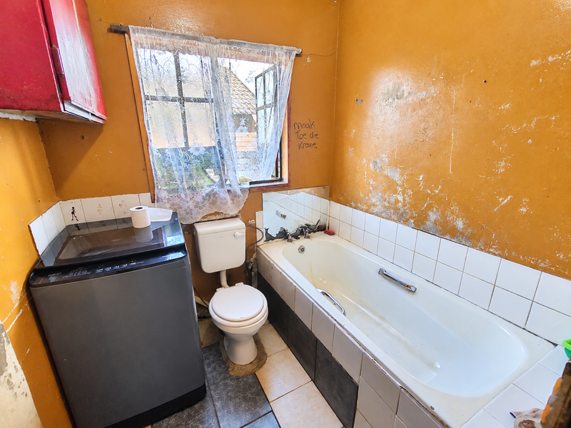 A dated bathroom featuring a bathtub, toilet, and tiled splashback, currently requiring significant wall repairs and cosmetic updates to improve the overall condition.