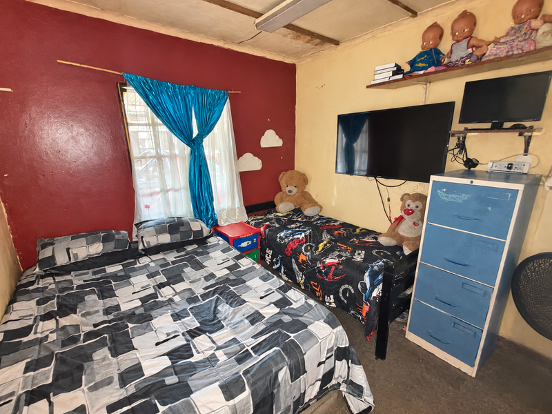 A bedroom featuring a dual-tone wall finish, a window with curtains, and a ceiling light fixture. The room requires cosmetic updates and wall repairs.