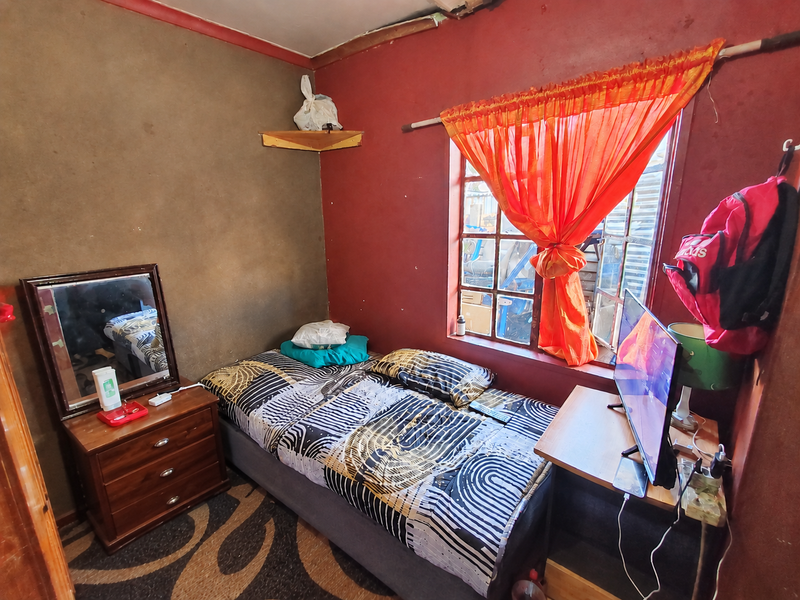A compact bedroom featuring a window with a curtain rod and painted walls showing signs of wear and surface deterioration.