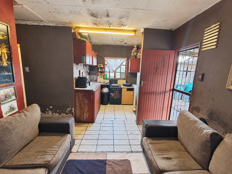 Open plan living and kitchen area featuring tiled floors, built-in cabinetry, and a freestanding stove, requiring significant cosmetic updates and ceiling repairs.
