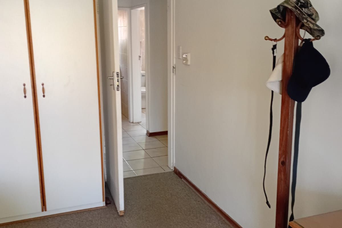 A bedroom featuring built-in cupboards and carpeted flooring, with a doorway leading to an adjacent tiled bathroom area.