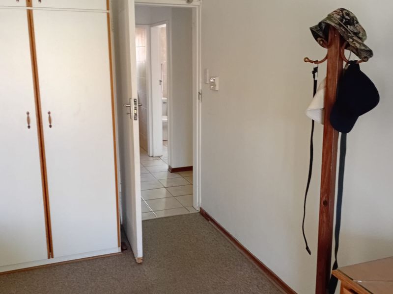 A bedroom featuring built-in cupboards and carpeted flooring, with a doorway leading to an adjacent tiled bathroom area.