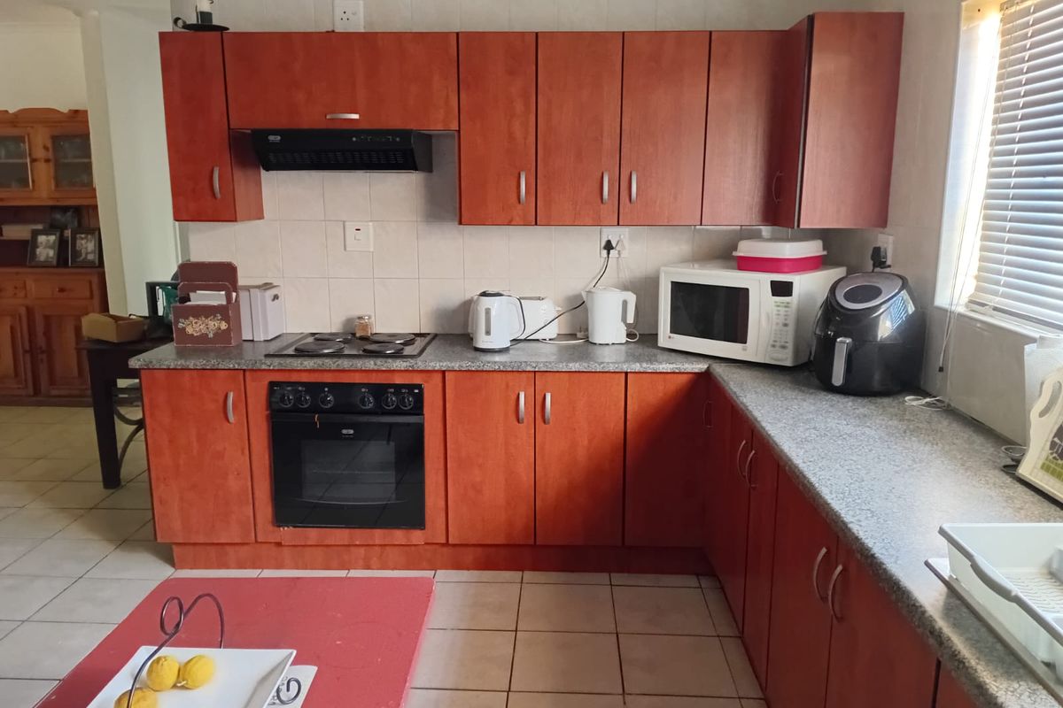 Functional kitchen featuring wood-look laminate cabinetry, granite-style countertops, built-in oven, electric hob, and tiled flooring, offering a practical layout for daily meal preparation.