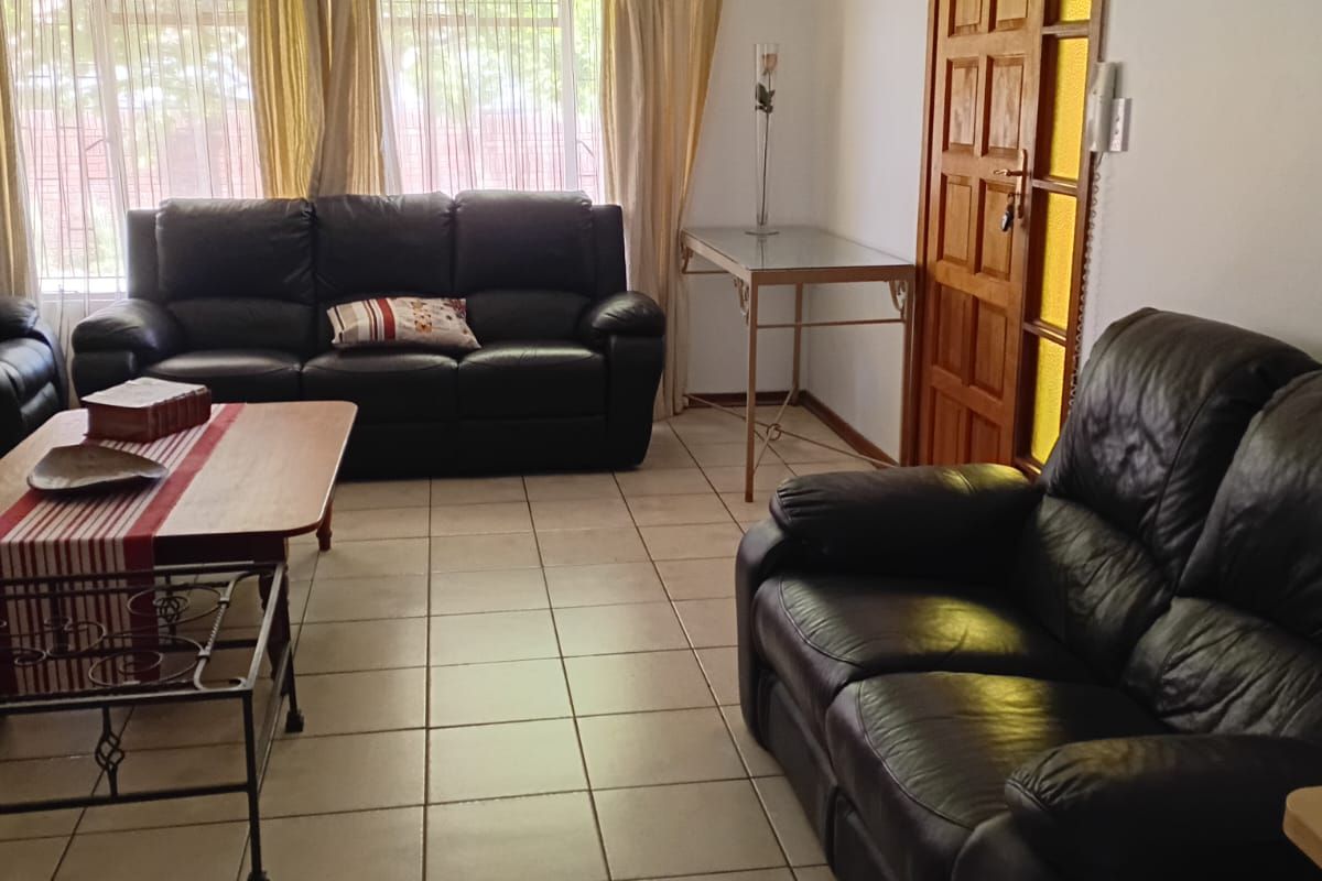 A living room featuring tiled flooring, a ceiling fan, and a timber panel door with security gate access.