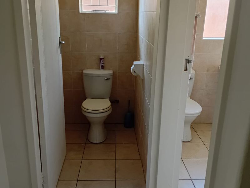 A functional bathroom featuring tiled walls and flooring, equipped with a standard toilet and a window with security bars.