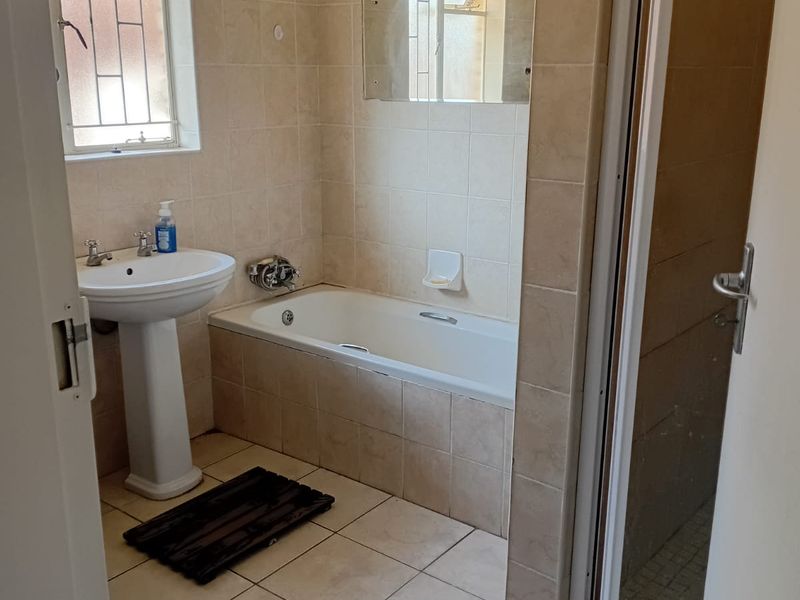 A functional bathroom featuring a pedestal basin, built-in bathtub, and separate shower enclosure with neutral ceramic tiling throughout.