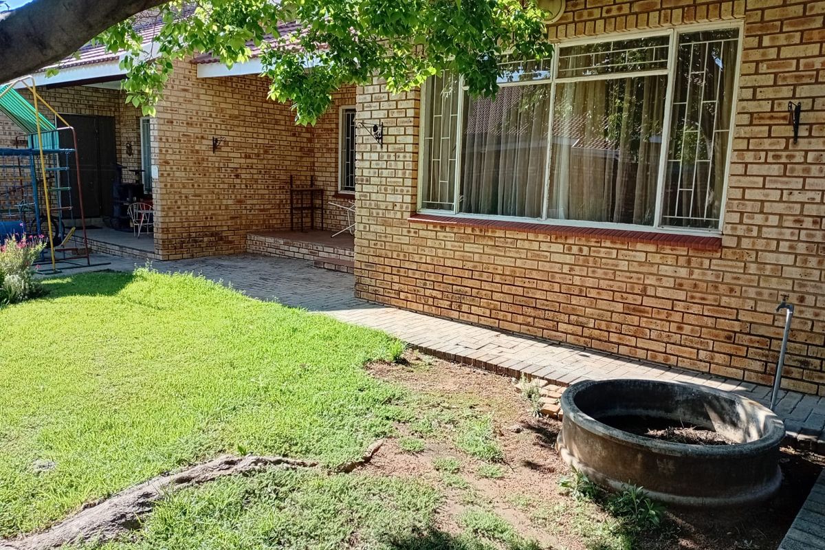 Rear exterior view of a face brick townhouse featuring a paved patio area, security bars on windows, and a garden space with a concrete planter.