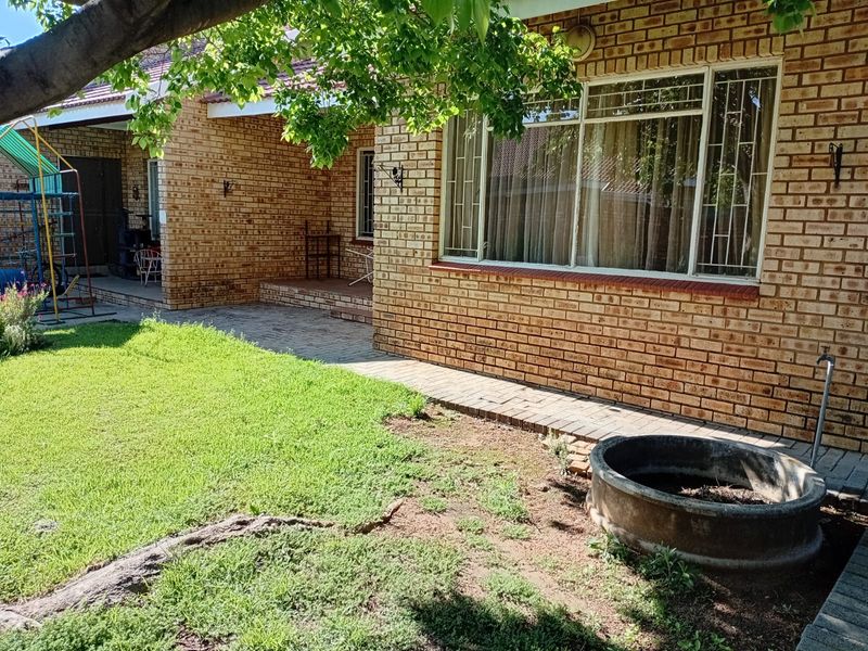 Rear exterior view of a face brick townhouse featuring a paved patio area, security bars on windows, and a garden space with a concrete planter.
