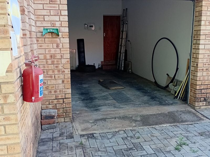 A functional single-car garage with brick exterior, concrete flooring, and paved driveway access, featuring a wall-mounted fire extinguisher.