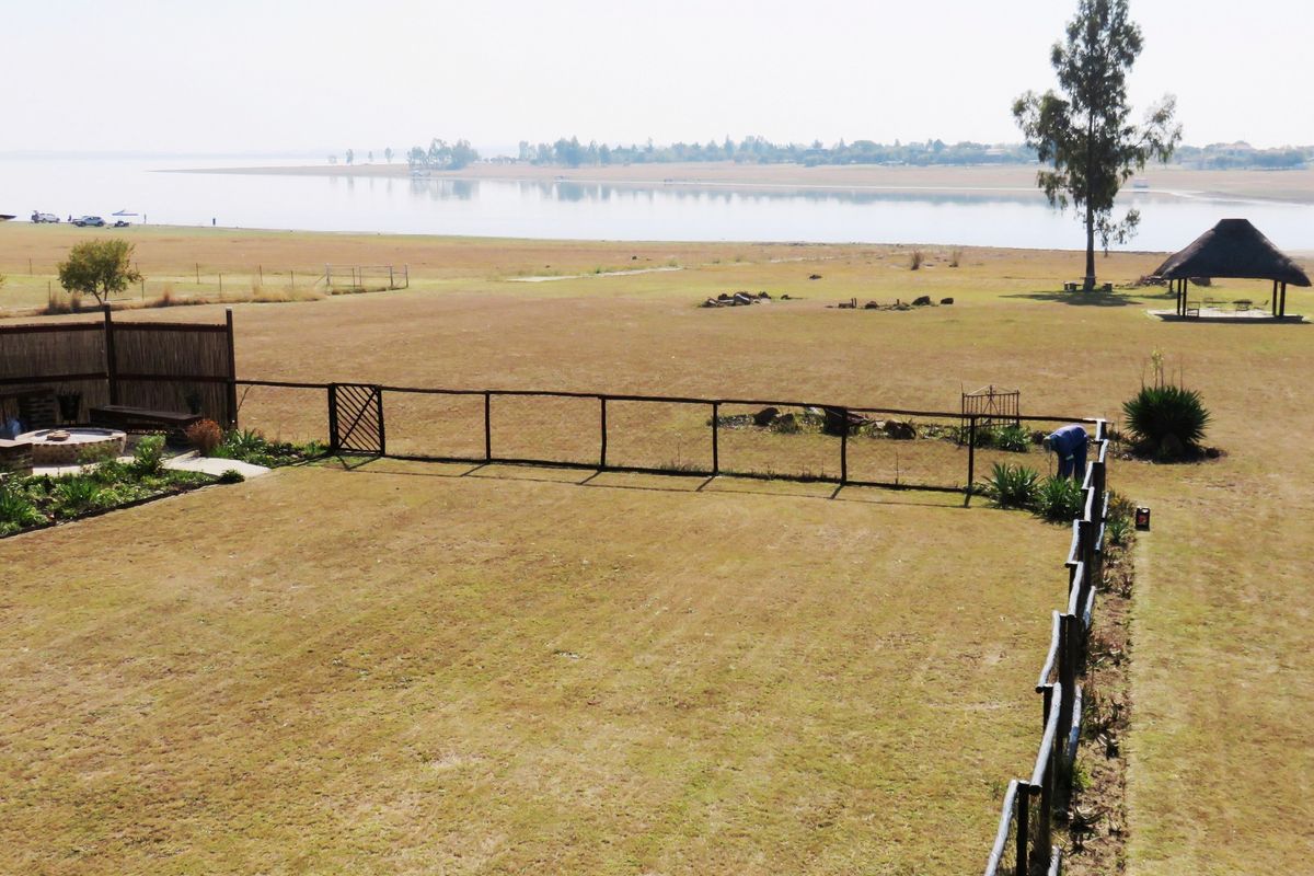 Aerial view of a spacious property featuring a large lawn, timber fencing, a fire pit area, and a thatched lapa overlooking the water.