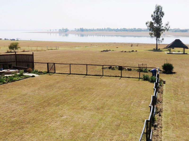 Aerial view of a spacious property featuring a large lawn, timber fencing, a fire pit area, and a thatched lapa overlooking the water.