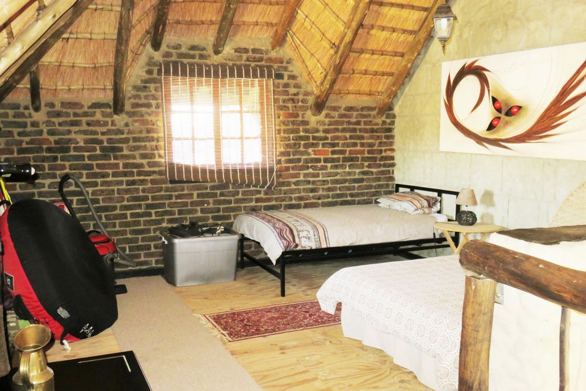 A rustic bedroom featuring exposed brick walls, a traditional thatched roof with timber rafters, and wooden flooring, creating a warm, character-filled living space.