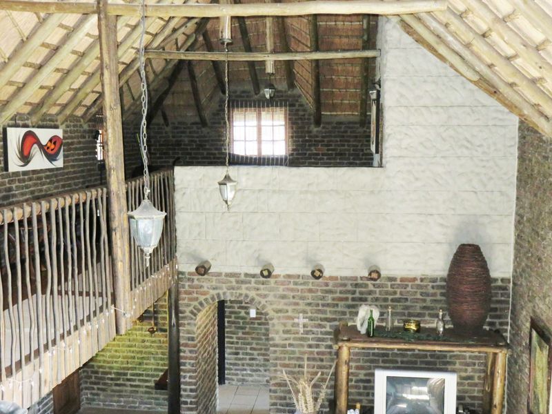 Spacious living area featuring a double-volume thatched roof, exposed brickwork, timber structural elements, and a mezzanine level overlooking the main space.