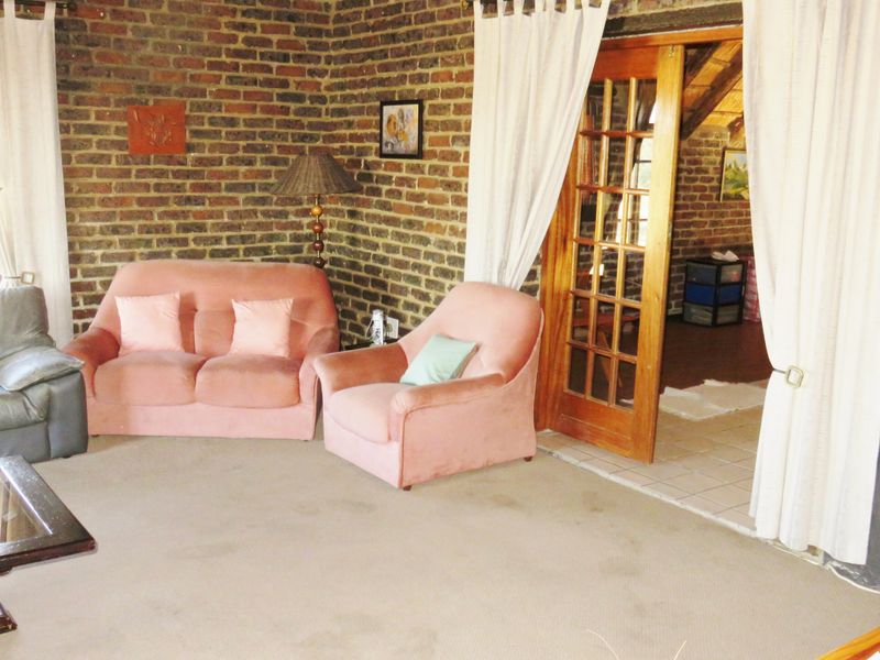 A living room featuring exposed brick walls, carpeted flooring, and wooden French doors leading to an adjacent space.