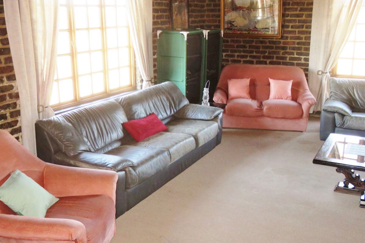 A living room featuring exposed brick walls, large timber-framed windows, and neutral carpeting, offering a classic aesthetic with potential for modern updates.