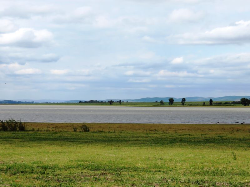 A scenic landscape view featuring a large body of water and open grassy fields under a cloudy sky.
