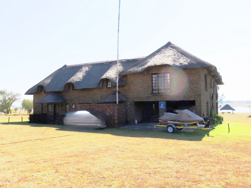 A traditional two-story house featuring a thatched roof and face brick exterior, with an integrated garage and expansive surrounding lawn.