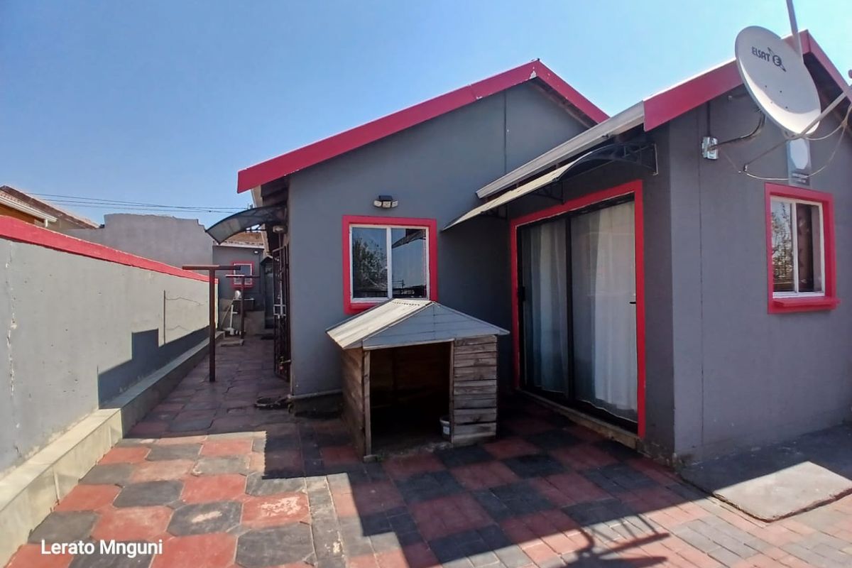 Rear exterior view of the house featuring a paved patio area, sliding glass doors, and a boundary wall.