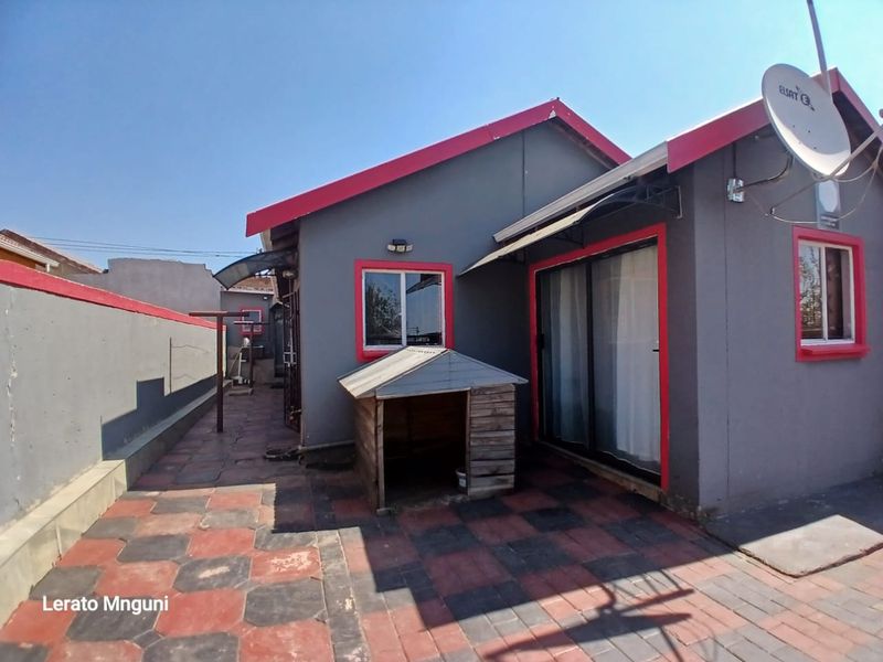 Rear exterior view of the house featuring a paved patio area, sliding glass doors, and a boundary wall.