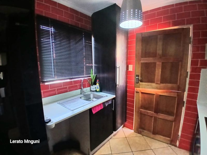 A functional scullery area featuring a stainless steel sink, dark built-in cabinetry, red tiled splashbacks, and a solid timber door.