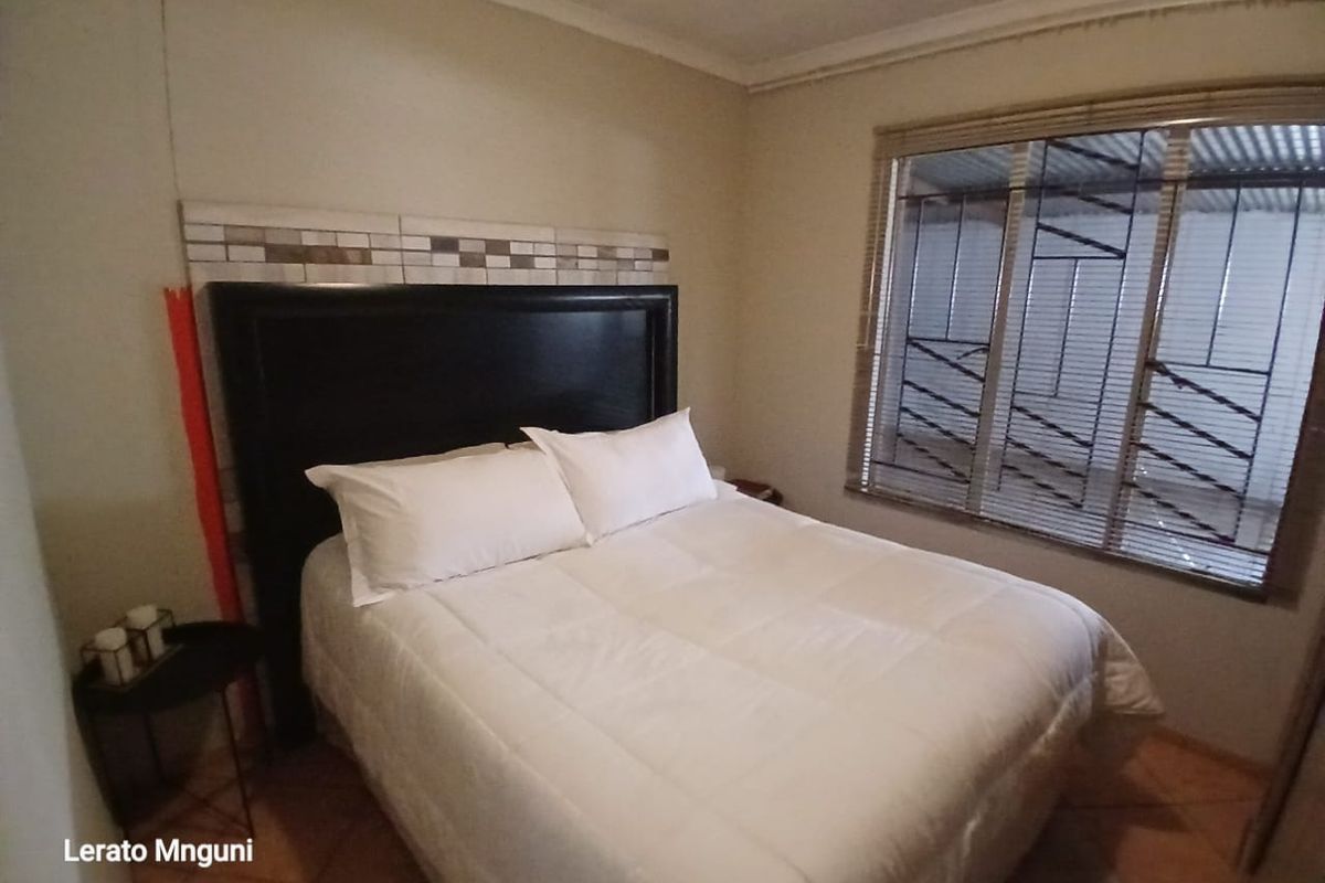 A functional bedroom featuring tiled flooring, security bars on the window, and a decorative tiled headboard feature wall.