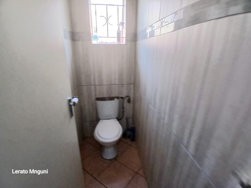 A compact guest bathroom featuring tiled walls, tiled flooring, and a standard toilet with a small window fitted with security bars.