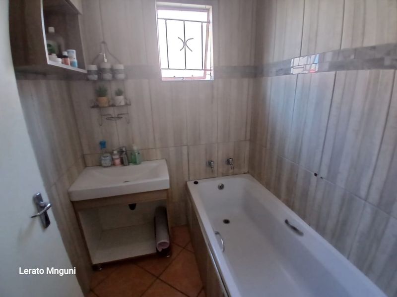 A compact bathroom featuring a built-in vanity with basin, a standard bathtub, and full-height wall tiling.