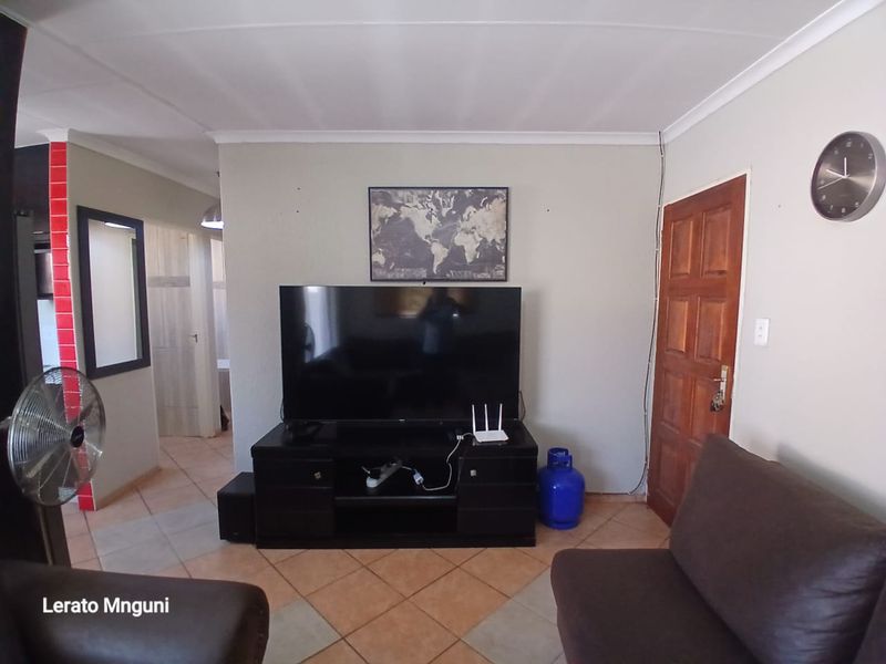 A living room featuring tiled flooring, a wooden door, and coved ceiling, with visible wall-mounted wiring.