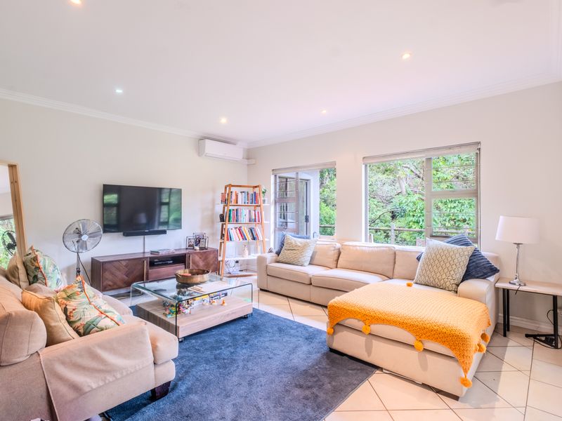 A bright and spacious living room featuring tiled flooring, recessed downlights, and large windows that provide natural light and views of the surrounding greenery.